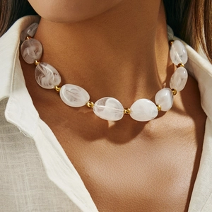 Dettaglio di perle in resina marmorizzata e sfere dorate su collana minimalista