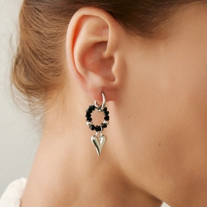 Close-up of a silver heart pendant earring with black faceted beads worn by a model