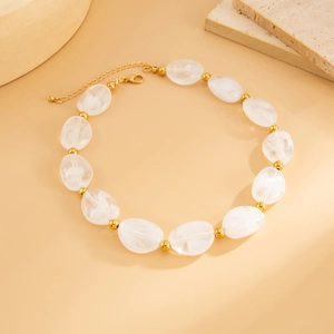 Dettaglio macro di perle in resina bianca traslucida con accenti dorati e chiusura a moschettone