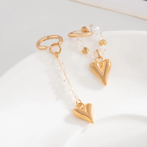 Detail of asymmetric gold earrings with crystal beads and heart pendants on white plate
