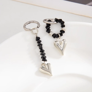 Detail of asymmetric black crystal and silver heart pendant earrings on white ceramic