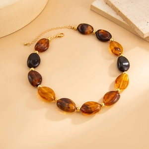 Dettaglio della collana in resina ambra e marrone con perline dorate e chiusura a moschettone