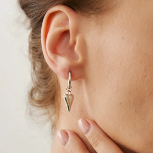 Detailed view of silver heart pendant earring worn by a model with soft lighting