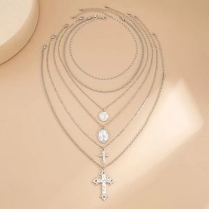 Set di collane d'argento a più strati con ciondoli a croce e moneta su sfondo beige