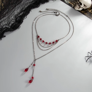 Gros plan d'un collier gothique à trois couches avec chaînes sombres et cristaux rouges