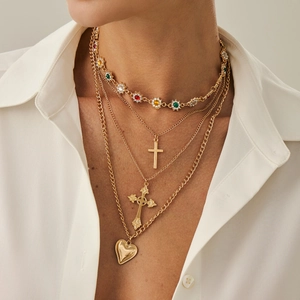 Dettaglio di collana multistrato dorata con croce, fiori di strass e cuore