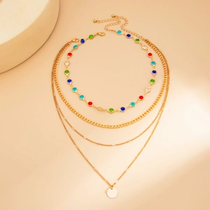 Dettaglio di collana dorata a strati con gemme colorate e ciondolo rotondo