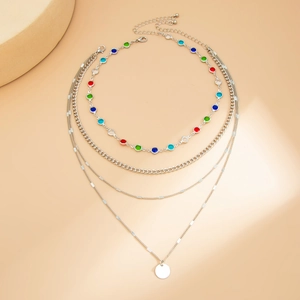 Collana multistrato argento con cristalli colorati e ciondolo rotondo su sfondo beige caldo