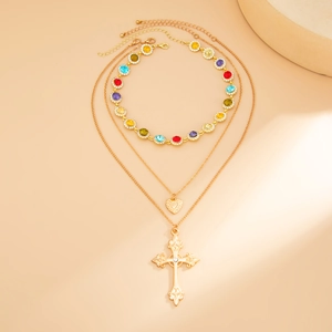 Dettaglio di collana tripla dorata con zirconi colorati e ciondolo a croce inciso