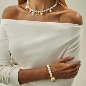 Dettaglio del set collana e bracciale di perle con ciondoli dorati a cuore e fiocco su modella