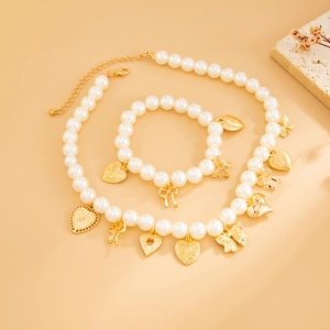Dettaglio parure collana e bracciale di perle con ciondoli dorati a cuore e fiocco