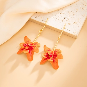 Detail of long floral drop earrings with red enamel petals and golden stems