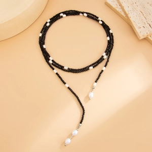Detail van de lange gelaagde ketting met zwarte facetkralen en barokke parels