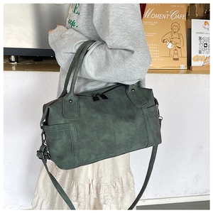 Dettaglio borsa Boston vintage verde scuro con tracolla regolabile e manici in un caffè