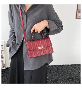 Detail of wine red woven leather crossbody bag with a gold twist lock and flap closure