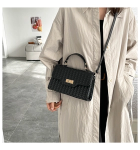 Detail of black woven texture handbag with gold twist lock worn with a trench coat