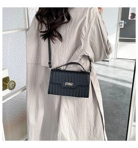 Detail of black woven texture shoulder bag with metal turn-lock and adjustable strap