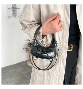 Dettaglio borsa a mano in vernice nera con fiocco decorativo e tracolla sottile