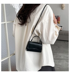 Dettaglio di una mini borsa nera con patta ondulata indossata su una camicia bianca pulita