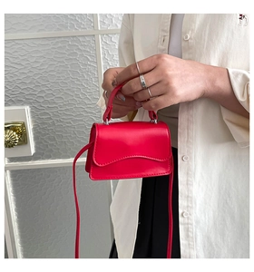 Dettaglio mini borsa rossa in pelle con patta a onde e manico tenuta da una modella