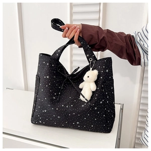 Dettaglio della borsa tote nera con stampe di stelle, fiocco e ciondolo orsetto di peluche