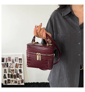 Detail of burgundy box bag with crocodile pattern and golden zippers held by a model