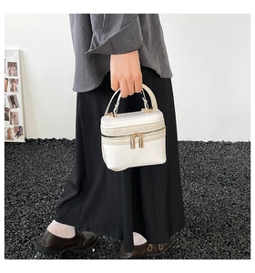 Detail of white crocodile pattern handbag with gold double zippers and top handle