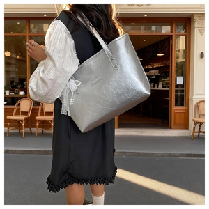 Dettaglio borsa metallizzata argento con pizzo, ciondolo di perle e texture a pieghe
