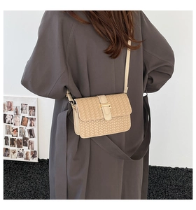 Dettaglio borsa a tracolla intrecciata beige con fibbia dorata indossata su cappotto grigio