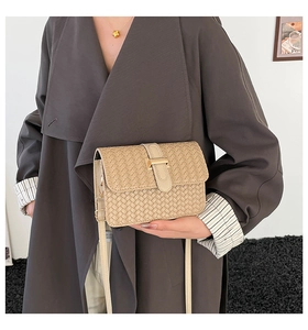 Dettaglio borsa a tracolla intrecciata beige con fibbia dorata su un trench grigio elegante