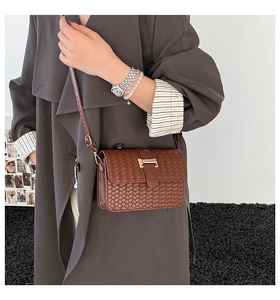 Dettaglio borsa a tracolla in pelle intrecciata marrone con fibbia dorata su cappotto grigio