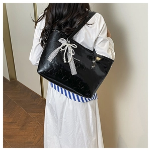 Dettaglio della borsa tote nera lucida con fiocco in pizzo e ciondoli di perle eleganti