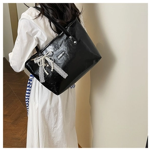 Dettaglio borsa tote in vernice nera con fiocco in pizzo bianco e ciondolo di perla
