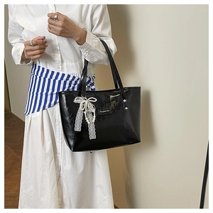 Dettaglio borsa tote in ecopelle nera con fiocco in pizzo e perle e logo in argento