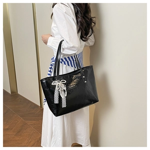 Dettaglio borsa tote in vernice nera con fiocco in pizzo e decorazione di perle