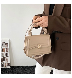 Dettaglio della borsa in pelle beige con manico annodato e chiusura a girello dorata