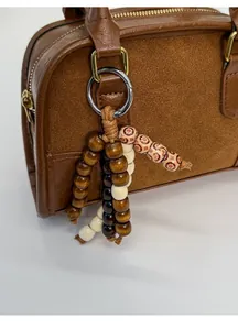 Dettaglio del ciondolo vintage con perline di legno su una borsa Boston in pelle marrone