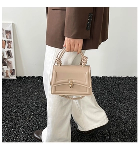 Dettaglio della borsa beige con manico a nodo e chiusura rotante dorata tonda