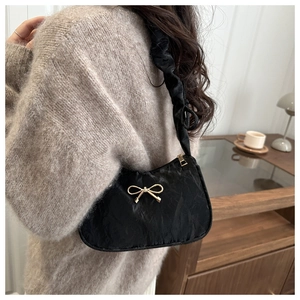 Close-up of black pleated hobo bag with a gold bow detail worn by a model in a cozy setting