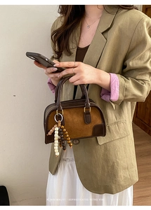 Borsa retrò in pelle bicolore con ciondolo in legno su sfondo di un blazer verde oliva