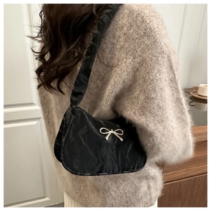 Détail du sac sous l'aisselle en nylon noir avec nœud doré porté par un modèle