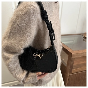 Detail view of black pleated underarm bag with gold bow ornament and cloud shoulder strap