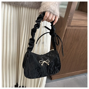 Gros plan d'un sac à main noir plissé avec nœud doré et poignée à volants sur modèle