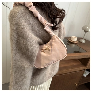 Detail of light pink pleated hobo bag with gold bow charm on shoulder strap
