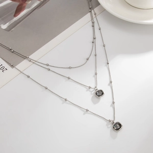 Close-up of a silver layered necklace with square grey crystal pendants on a desk