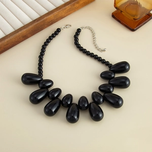 Dettaglio della collana con pendente a goccia in resina nera e catena di perle lucide