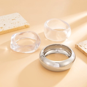 Minimalist wide acrylic transparent bangles and shiny silver metal bracelet on stone tray