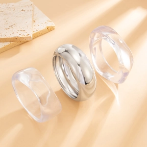 Close-up of polished silver metal and clear resin wide rings on a textured background