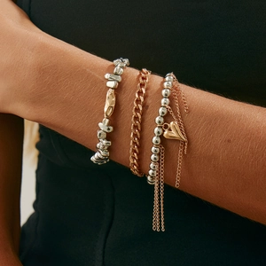 Detail eines Lagenarmband-Sets mit silbernen Perlen und goldenem Herz-Quastenanhänger