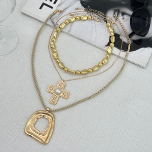 Dettaglio del set di collane dorate con croce di perle e pendenti geometrici su grigio
